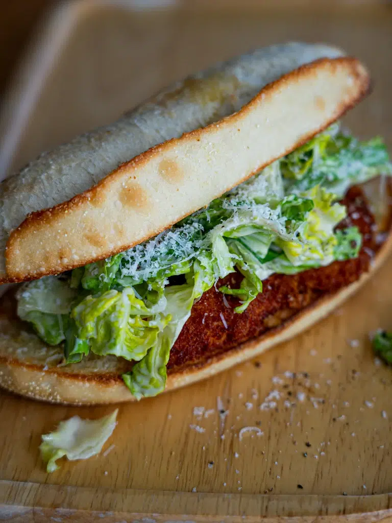 Close-up of a Crispy Chicken Caesar Sandwich with golden fried chicken, lettuce, and Caesar dressing in a toasted bun.