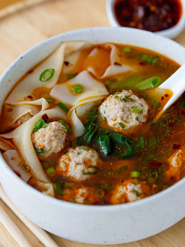 Plated deconstructed wonton soup captured from a sideways angle with visible ingredients.
