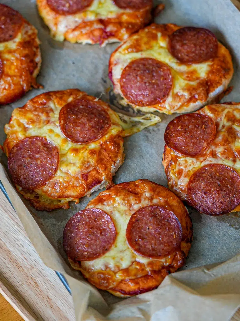 Freshly baked mini pizzas on a tray, topped with shredded mozzarella cheese, and pepperoni.